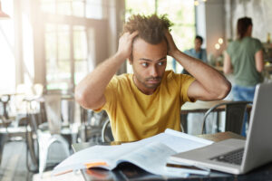 international afro american student feeling stressed, keeping hands on his head, staring at laptop screen in frustration and despair after he made serious mistake in calculation, working on research